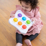 Child in a pink dress and gray leggings playing with Fat Brain Toy Cos colorful Dimpl Duo, engaging in tactile learning.