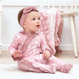 A baby in Tesa Babes Wild West Pink romper sits on a white rug, with an ultra-soft blanket draped over a chair.