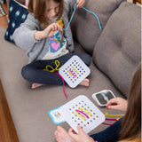 Two girls on a couch enjoy the creative fun of Sew Fast by Fat Brain Toy Co, threading strings through pegboards and tackling challenge cards.