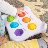 A baby learns shapes with Dimpl Duo by Fat Brain Toy Co, playing with colorful buttons marked circle, triangle, square, diamond, and oval.