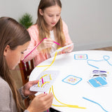 Two girls sit at a table, immersed in Sew Fast by Fat Brain Toy Co, threading colorful strings through challenge cards for fun.