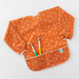 Bumkins Long-Sleeved Art Smock: Grounded holds two paintbrushes in the front pocket, laying flat on a white background.