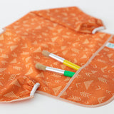 Close-up of Bumkins Long-Sleeved Art Smock: Grounded on a white background, with paintbrushes in the pocket.