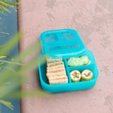 A bento box from Bumkins Lunchbox Legends 6-Piece Set: Ocean Blue Jelly with snacks rests on tan concrete.