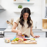 In the kitchen, a woman organizes snacks into a Bumkins Silicone Bento Box 3 Section: Pink Jelly on a fruit-lined counter.
