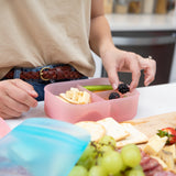 A person meal-preps a Bumkins Silicone Bento Box 3 Section: Pink Jelly with blackberries and cheese on a kitchen counter.