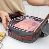 A person puts a Bumkins Silicone Bento Box 3 Section: Pink Jelly into a gray insulated lunch bag on a kitchen counter.