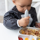 A child enjoys pasta and strawberries from a divided plate while wearing a Bumkins Sleeved Bib: Jack Skellington.