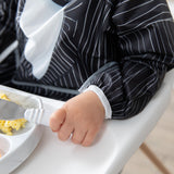 A child in a high chair wears a Bumkins Sleeved Bib: Jack Skellington, holding a fork near scrambled eggs.