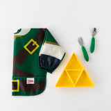 Bumkins Spoon + Fork: Jade sits near a yellow triangle-shaped plate and a folded green tunic-style bib on a white background.