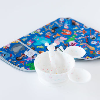 Bumkins Silicone First Feeding Set: Mickey Mouse Vanilla Sprinkle sits on a white background next to a brightly colored bib.