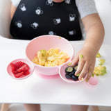 A child in a high chair enjoys scrambled eggs from a Bumkins Silicone First Feeding Set: Minnie Mouse Light Pink, with berries on the side.