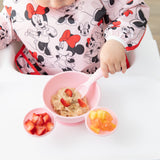 A child enjoys oatmeal with strawberries from a Bumkins Silicone First Feeding Set: Minnie Mouse Light Pink while seated in a high chair.
