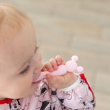 A baby in a bib chews on a spoon from Bumkins Silicone First Feeding Set: Minnie Mouse Light Pink.