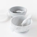 Bumkins Silicone First Feeding Set: Marble sits in front of a gray bowl and spoon set on a white background.