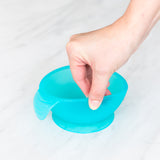 A hand holds a Bumkins Silicone First Feeding Set: Blue Jelly, demonstrating the suction cup bottom on a marble surface.