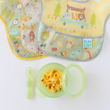 Bumkins Silicone First Feeding Set: Green Jelly filled with scrambled eggs and bacon bits sits near 3 waterproof bibs on a white background.