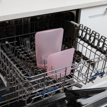 Bumkins Silicone Flat Reusable Bag 2 Pack, Pink sits in the top rack of an open dishwasher.