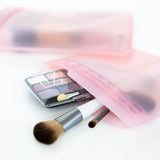 Makeup brushes and an eyeshadow palette peek out from Bumkins Silicone Flat Reusable Bag 2 Pack, Pink on a white background.