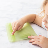 A child exploring a Bumkins Silicone Flat Reusable Bag 2 Pack, Sage on a marble countertop.