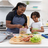 A woman and child prepare lunch using Bumkins Silicone Flat Reusable Bag 2 Pack, Sage at a kitchen counter surrounded by fresh ingredients.