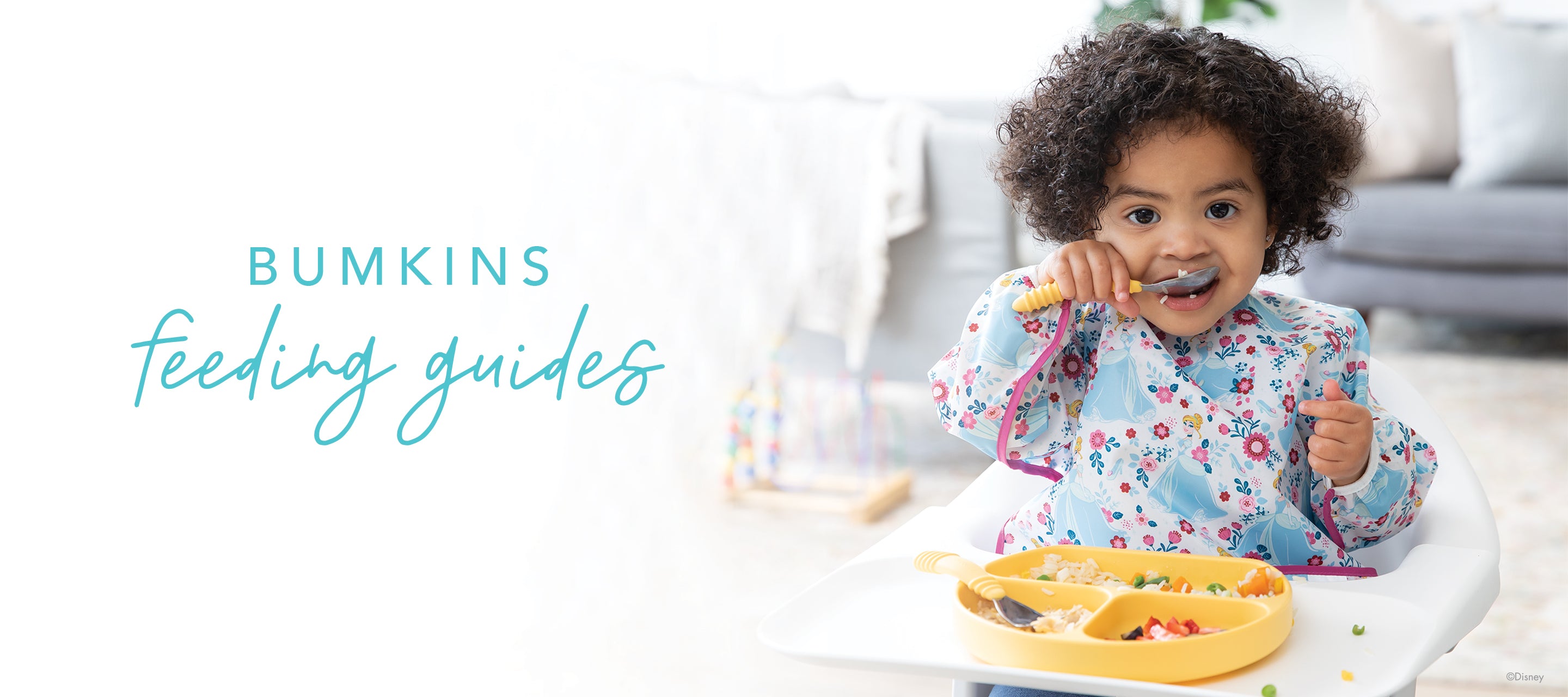 A toddler with curly hair is sitting in a high chair, wearing a floral bib, and holding a fork while eating from a divided yellow plate. The text on the image reads Bumkins feeding guides. The background shows a cozy living room.