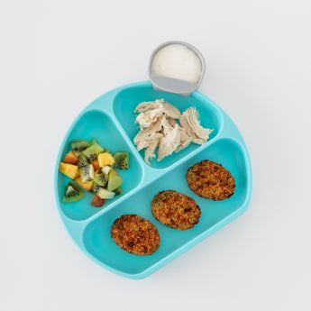 Bumkins Silicone Grip Dish: Blue holds chicken, fruit salad, and falafel on a white background, with a gray cup of white dip.