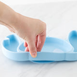 A hand holds a Bumkins Silicone Grip Dish: Stitch, demonstrating the suction cup bottom on a marble surface.