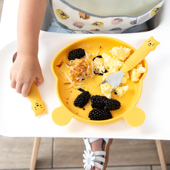 Close-up of a child in a high chair eating berries and eggs with Bumkins Grip Dish Essential 3-Piece Mealtime Set: Disney Winnie the Pooh.