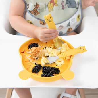 Close-up of a child in a high chair eating breakfast with Bumkins Grip Dish Essential 3-Piece Mealtime Set: Disney Winnie the Pooh.