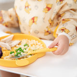 Close-up of a child in a sleeved bib eating with Bumkins Grip Dish Essential 3-Piece Mealtime Set: Disney Winnie the Pooh.