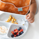 Close-up of a toddler in an orange bib enjoying fruit and yogurt with Bumkins Grip Dish Essential Infant 4-Piece Mealtime Set: Marble.