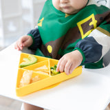 A child in a high chair enjoys avocado, broccoli, and snacks from a Bumkins Silicone Grip Dish: Zelda™ Triforce on the tray.