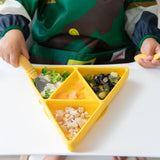 A child enjoys snacks from a Bumkins Silicone Grip Dish: Zelda™ Triforce filled with broccoli, fruit, and chicken on a high chair tray.
