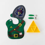 Bumkins Silicone Grip Dish: Zelda™ Triforce sits next to green handle utensils and a waterproof bib with a cape on a white background.