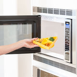 A hand places a Bumkins Silicone Grip Dish: Zelda™ Triforce, with pasta and veggies, into an open microwave.
