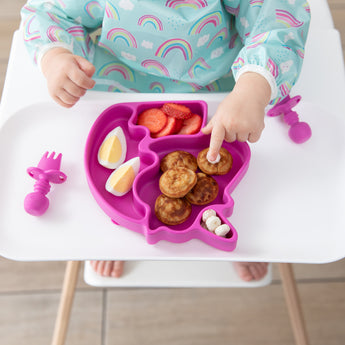 A child's hand reaches for mini pancakes from a Bumkins Silicone Grip Dish Special Edition: Unicorn on a high chair tray.