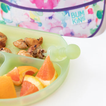 Close-up of a Bumkins Silicone Grip Dish: Green Jelly with orange slices & pancakes and a matching toddler spoon on a high chair tray.
