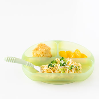 Bumkins Silicone Grip Dish: Green Jelly holds pasta, broccoli, mandarins, and cornbread with a fork on a white background.