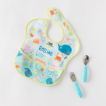 A Bumkins SuperBib® and Sleeved Bib 3-Piece Set: Rolling With The Waves, Whale Tail, Ocean Life lays with blue utensils on a white background.