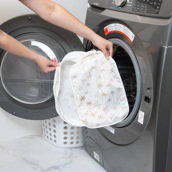 A person holds a Bumkins Packing Cube 2 Pack: Palm Daze in front of a front-loading washing machine.