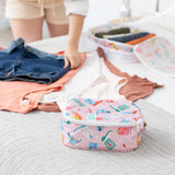 A person uses Bumkins Packing Cube 2 Pack: Boots to neatly organize clothes on a bed.