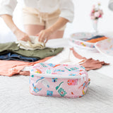 The Bumkins Packing Cube 2 Pack + Clear Travel Bag 3 Pack Set: Boots, in pastel prints, sits on a bed as clothes are folded.