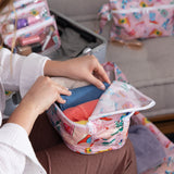 Someone packs colorful clothes into Bumkins Packing Cube 2 Pack: Boots while an open suitcase sits in the background.
