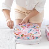 Wearing light clothes, a person packs items into a pink Bumkins Boots set—Packing Cube 2 Pack + Clear Travel Bag 3 Pack.