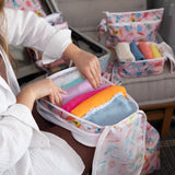 A person packing colorful clothes into a Bumkins Packing Cube 2 Pack: Boots made from waterproof fabric, with more organizers nearby.