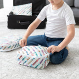 A child sits on a carpet, zipping a Bumkins Packing Cube 2 Pack: Mickey & Friends Varsity with an open suitcase in background.