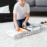 A child organizes clothes in Bumkins Packing Cube 2 Pack: Mickey & Friends Varsity, with a couch and suitcase in the background.