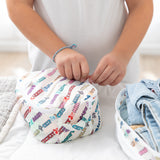 A child packs zips Bumkins Packing Cube 2 Pack: Mickey & Friends Varsity on a white bed next to packed clothes.