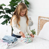 A girl in a white sweater packs clothes into Bumkins Packing Cube 2 Pack: Mickey & Friends Varsity on a bed.